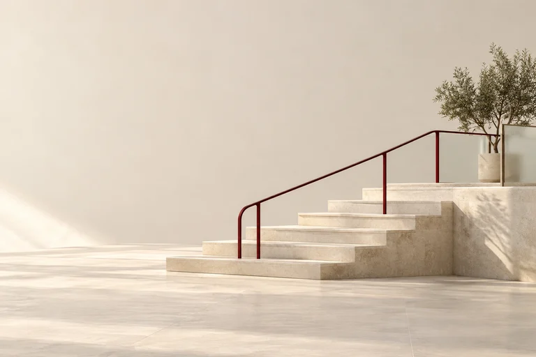 A gently rising stone stairway has a continuous burgundy handrail.
