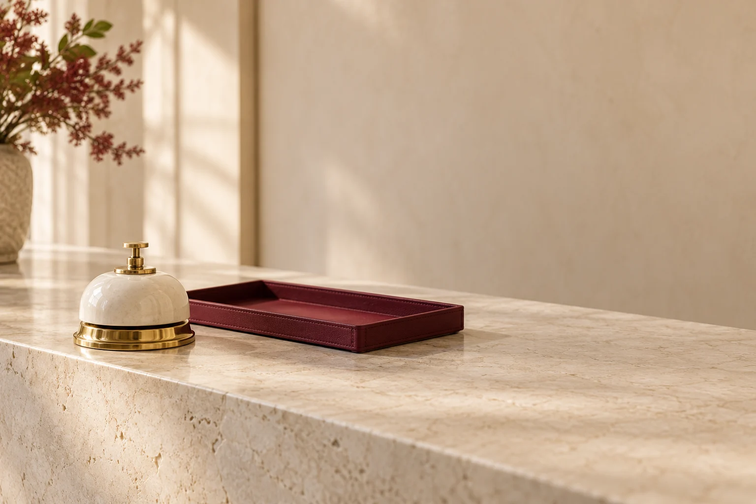 An ivory service bell beside a burgundy tray on a quiet limestone counter.