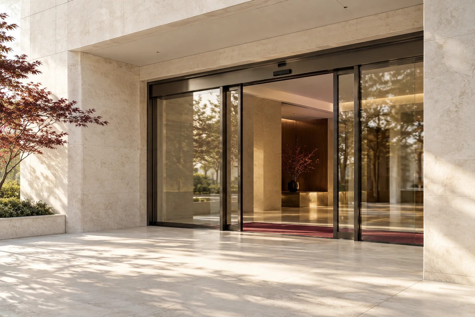An elegant automatic sliding glass entrance in a broad pale stone facade, doors slightly open, a restrained burgundy threshold detail, no people or signage.