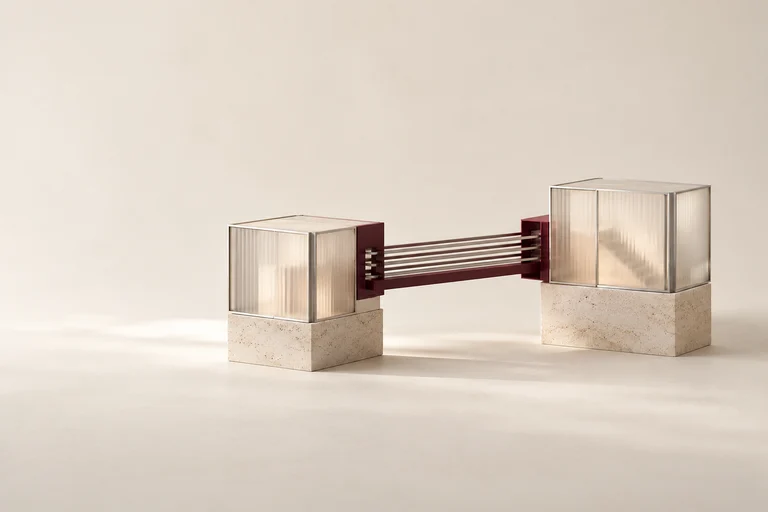 A burgundy bridge connects two glass modules on stone bases.