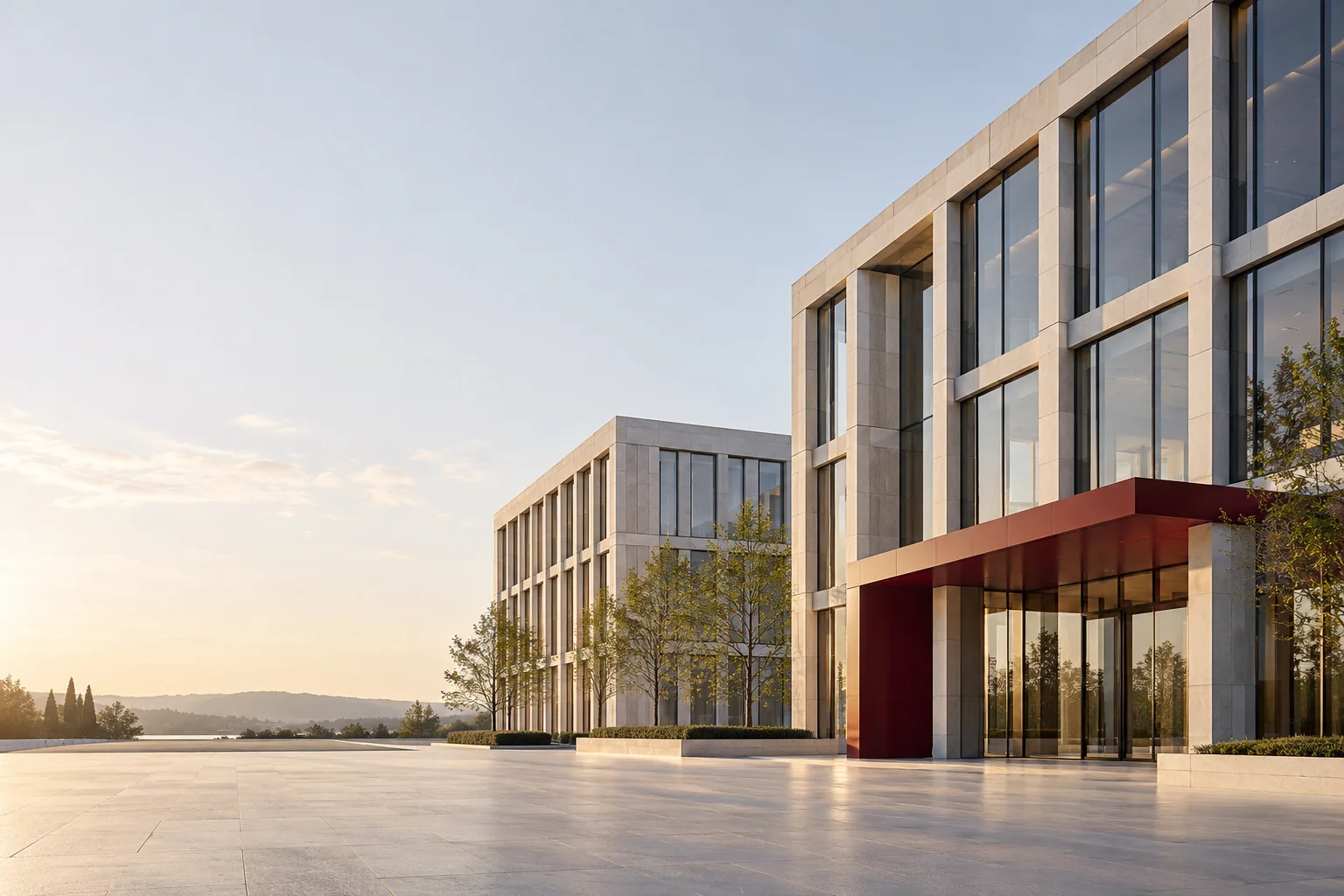 A large office campus with a burgundy entrance canopy across an open pale plaza.