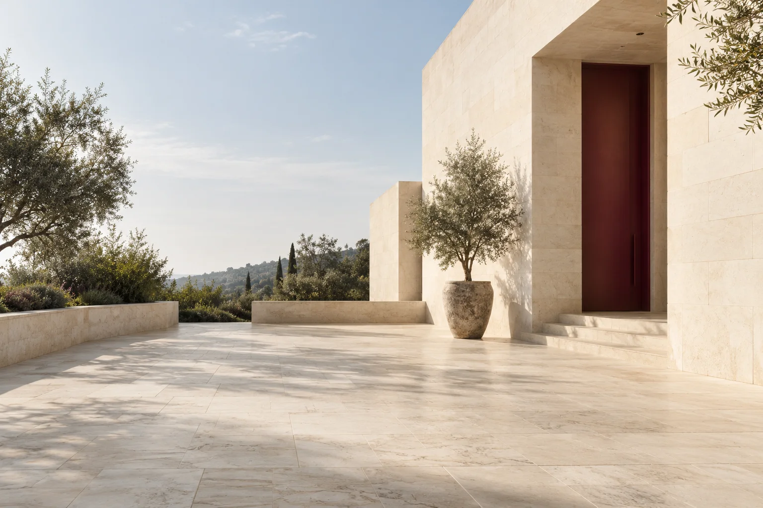 A quiet courtyard of a contemporary pale limestone building, one recessed burgundy entrance door, open sky and expansive immaculate stone foreground.