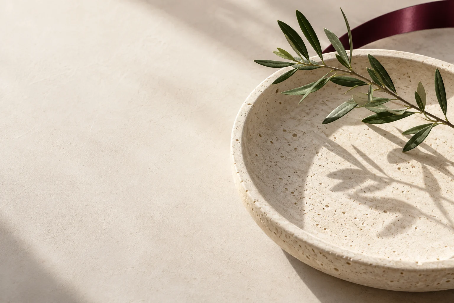 An olive branch above a circular stone dish with a discreet burgundy edge.