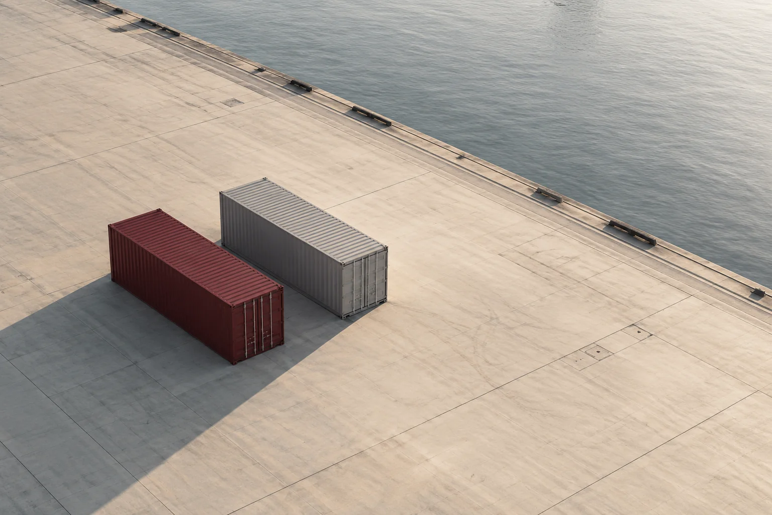 Burgundy and grey shipping containers on an expansive, quiet concrete quay.